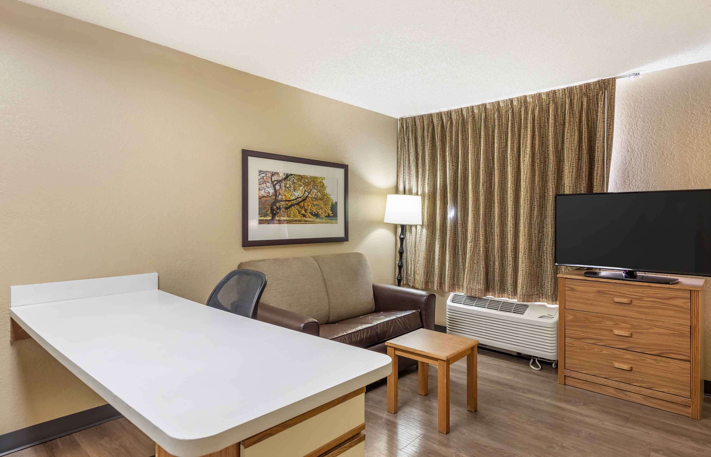 A hotel room with a desk, a sofa, a television, a lamp, and a window with curtains.