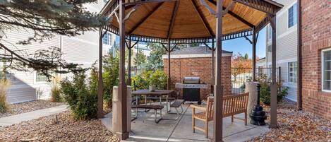 A covered patio with a grill, picnic table, and seating area.