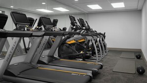 En rad löpband med digitala skärmar, placerade i ett gym med en vägg och ett tak som består av speglar.