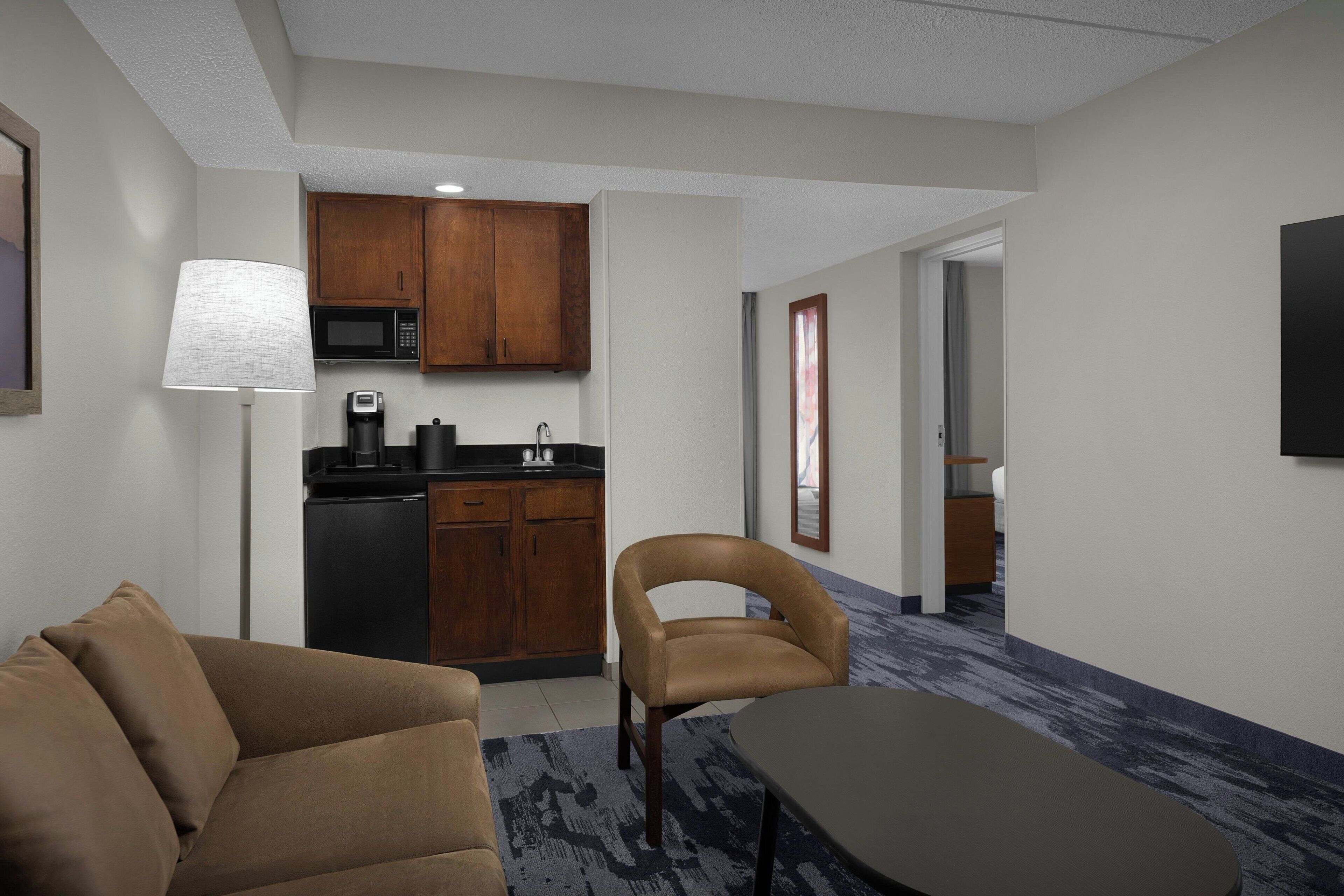 Habitación de hotel compacta con kitchenette, sofá, silla y una mesita.