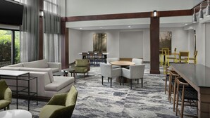 En modern hotellobby med en stor sittgrupp, ett matbord och en tv som är monterad på väggen.
