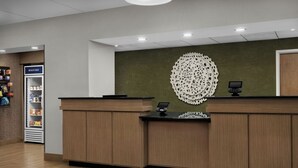 Ett välkomstområde med en receptionsdisk i trä, ett dekorativt väggobjekt och en kylmonter.