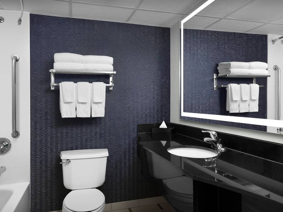 A modern bathroom with a white toilet, a black sink, and a mirror above the sink. There are two towel racks with white towels on them.