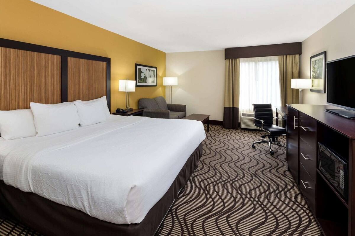 Une chambre d’hôtel avec un grand lit, un bureau, une chaise, une télévision et une fenêtre avec des rideaux.