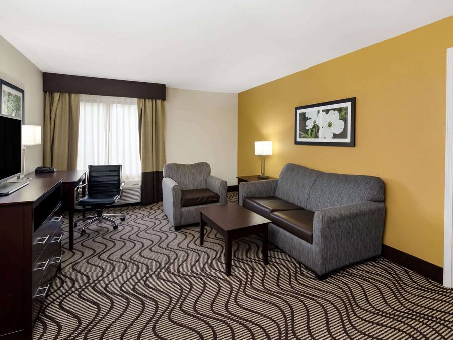 Une chambre d’hôtel avec un canapé, deux fauteuils, un bureau avec un ordinateur, une lampe et un tableau encadré au mur.