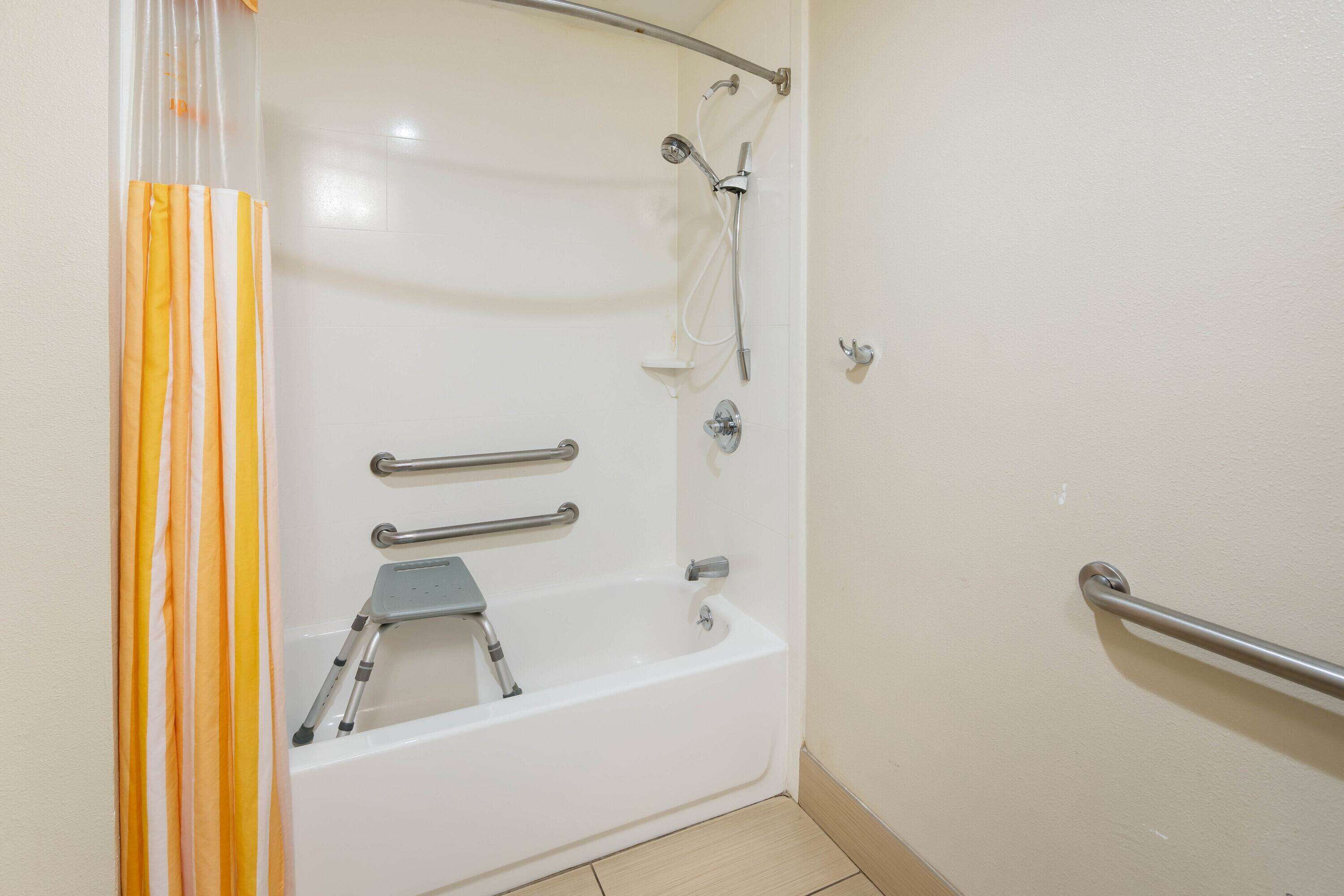 Baño con bañera blanca, ducha y retrete. Cuenta con barras de apoyo para mayor seguridad.