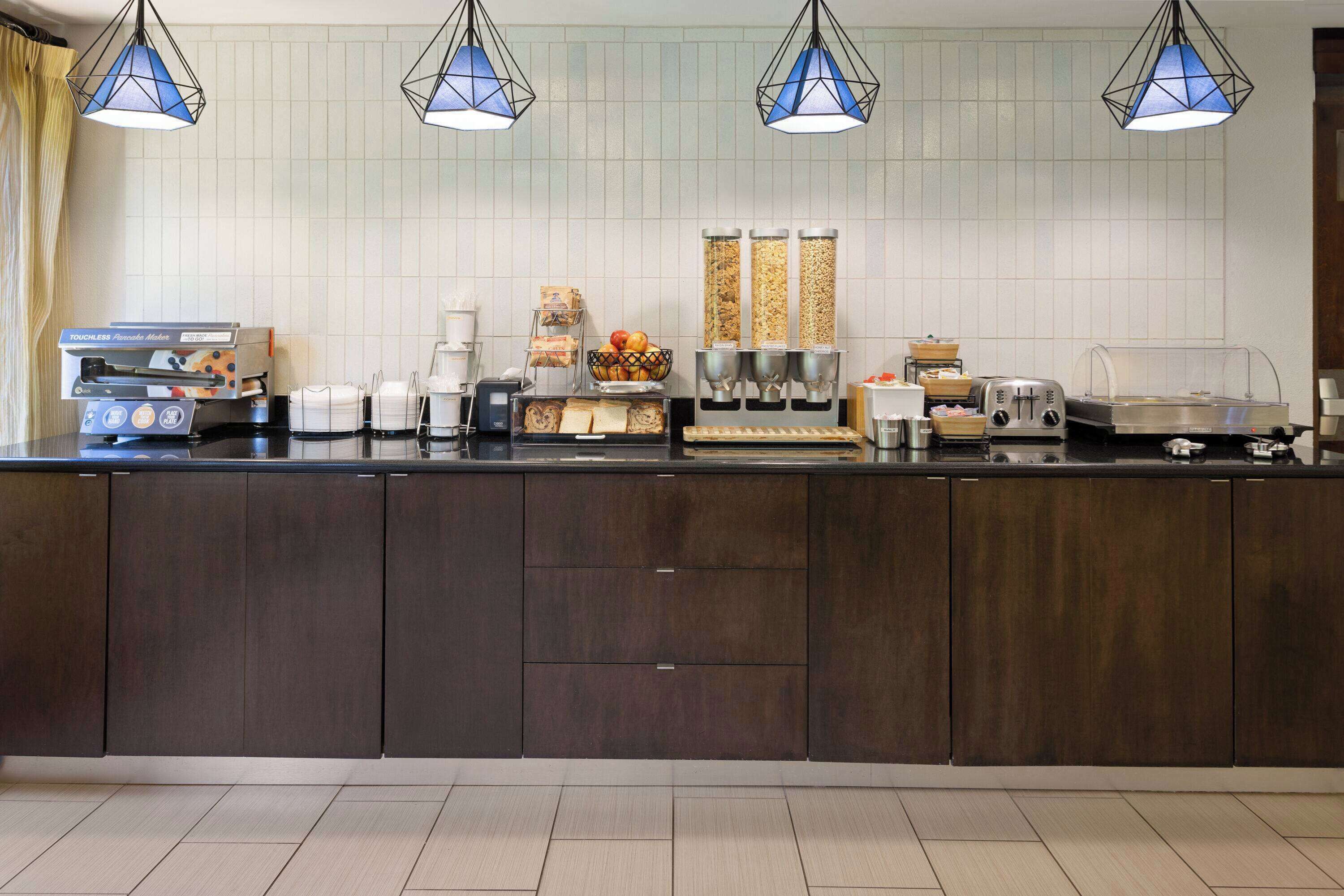 Una cocina moderna con un mueble de madera oscura, una cafetera, un tostador y un frutero.