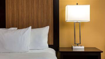 Una cama bien hecha con sábanas y almohadas blancas, un cabecero de madera y una mesita de noche con lámpara.