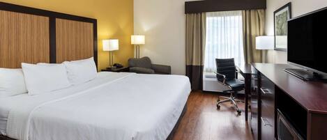 A hotel room with a large bed, a desk with a TV, a chair, and a desk lamp.