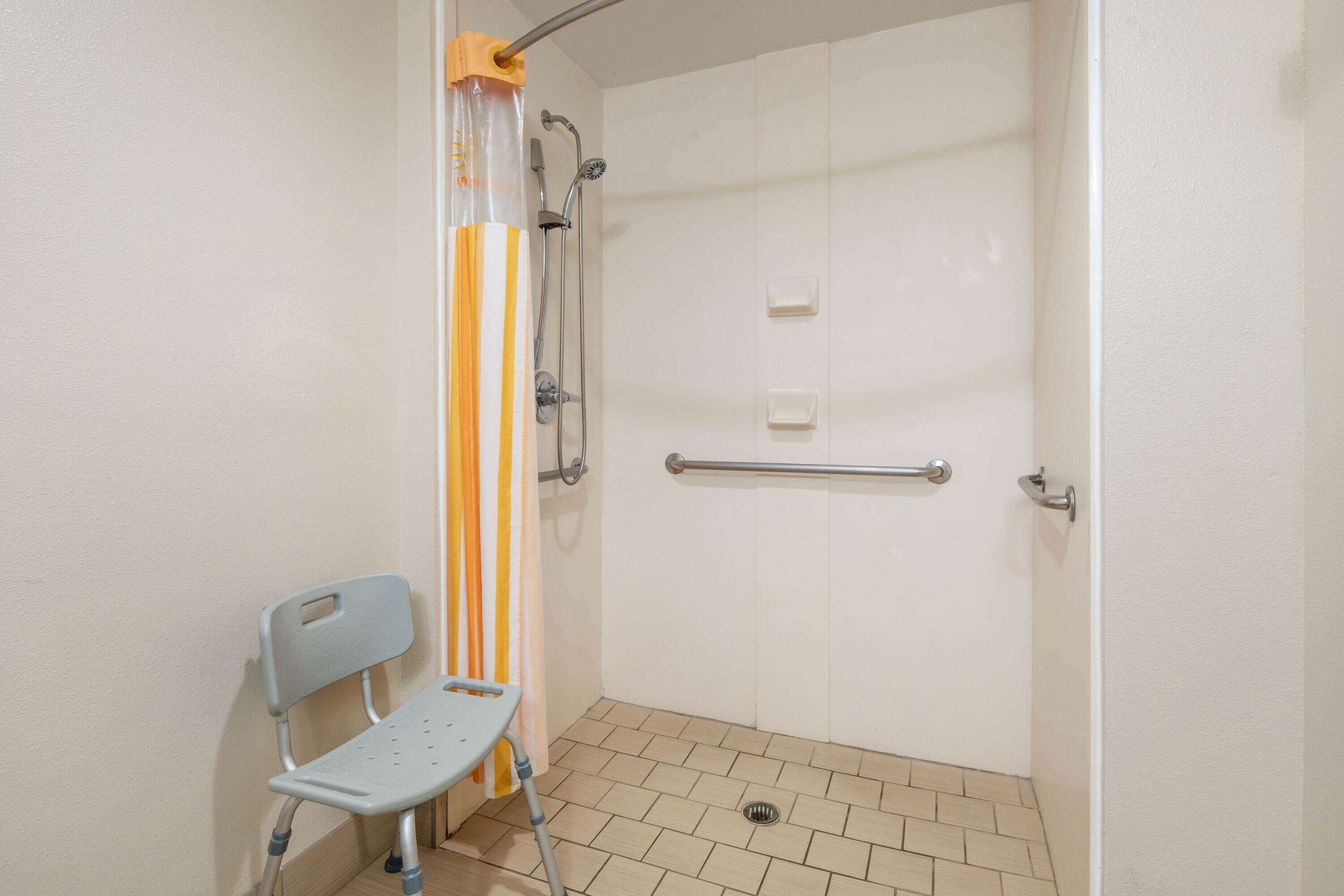 A shower area with a grab bar, a chair, and a striped shower curtain.