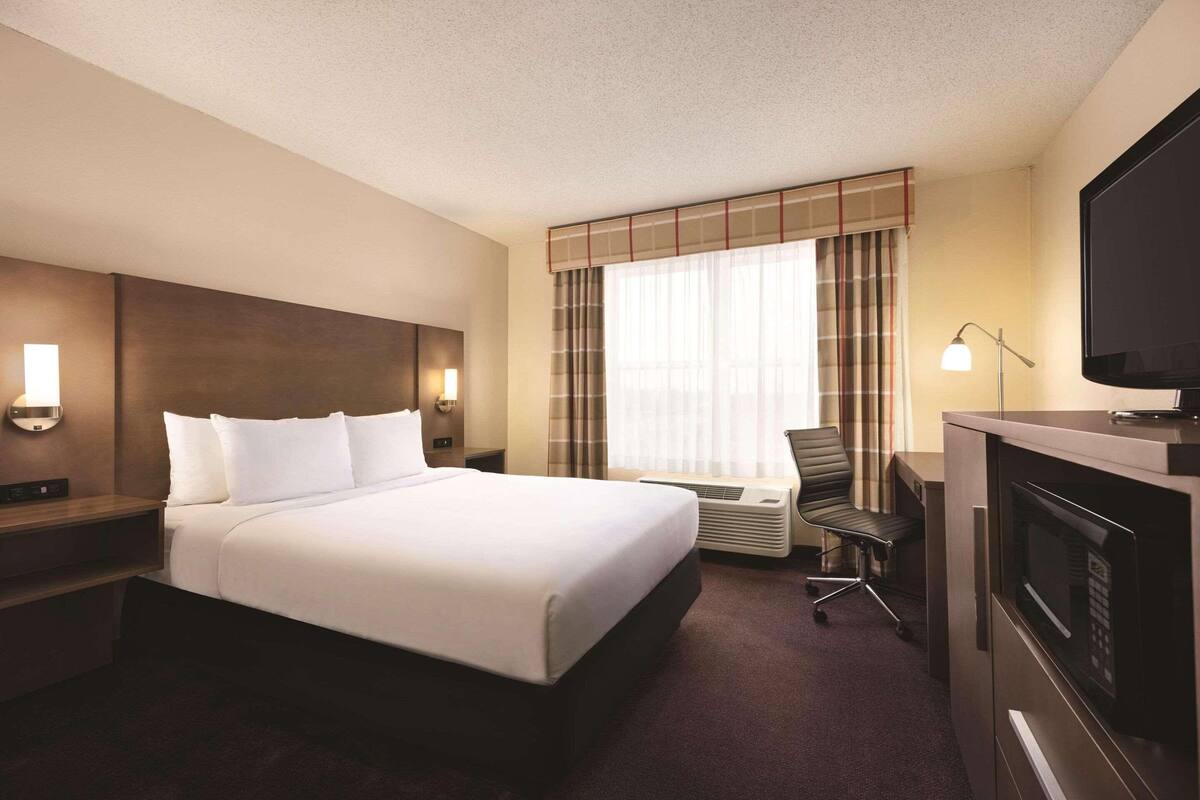 Ein Hotelzimmer mit einem großen Bett, einem Schreibtisch mit Stuhl, einem Flachbildfernseher und einer Mikrowelle.