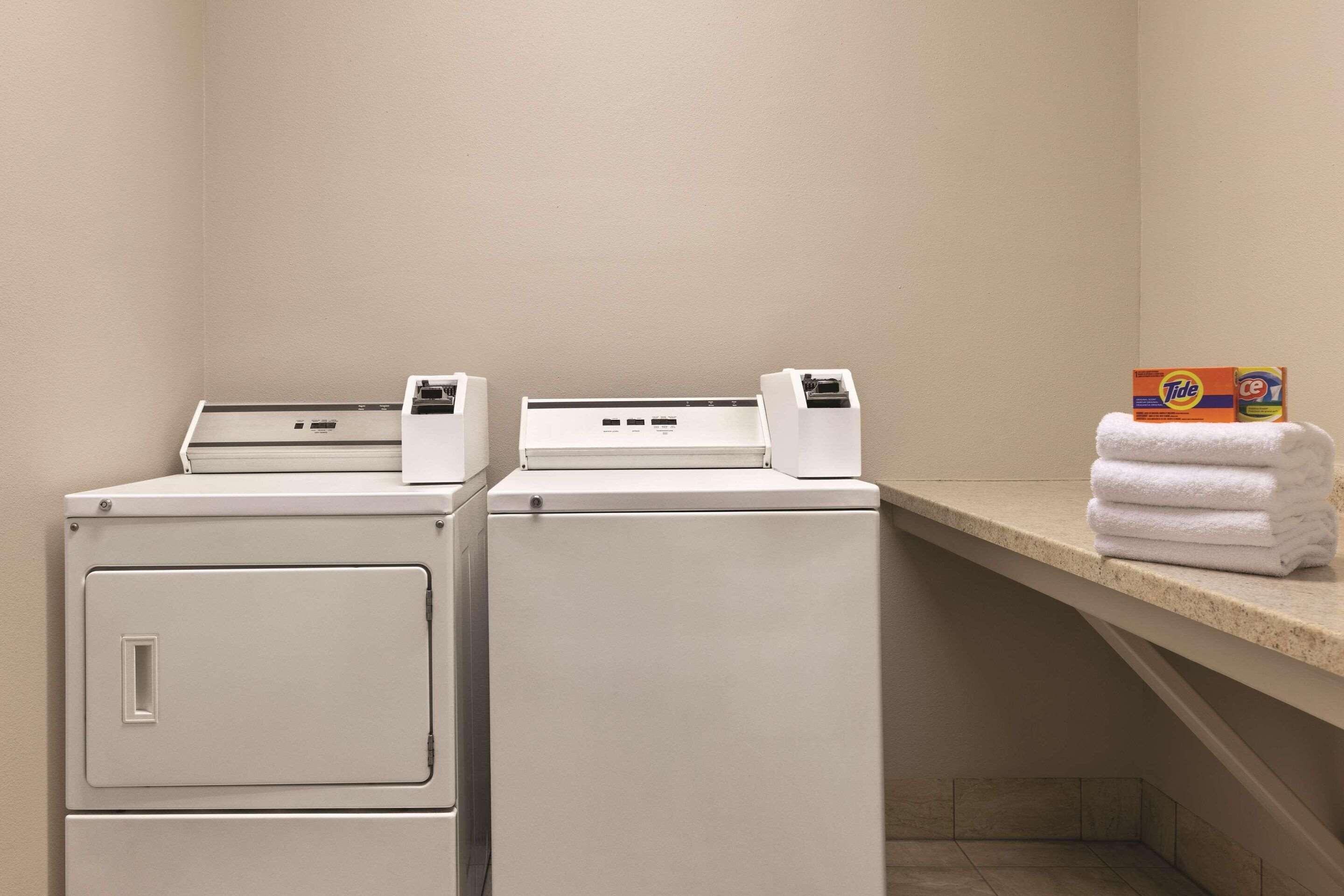 A laundry area with two washing machines and a shelf with folded towels and laundry detergent boxes.