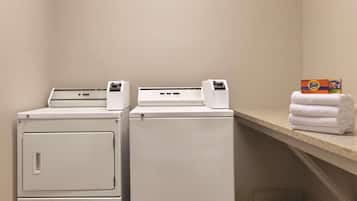 A laundry area with two washing machines and a shelf with folded towels and laundry detergent boxes.