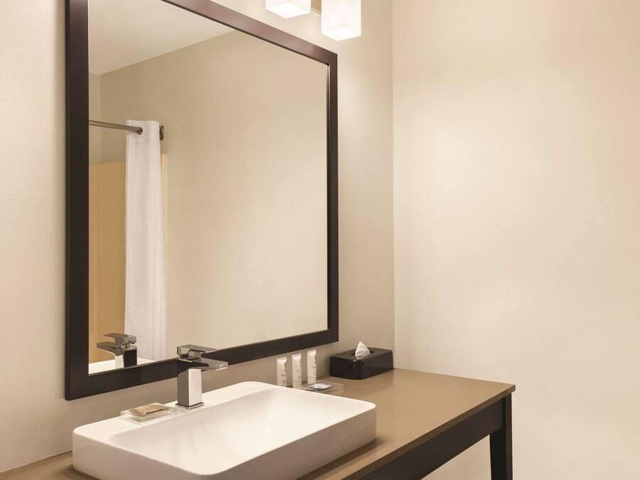 A modern bathroom with a large mirror, a white sink, and a small black tray with toiletries.