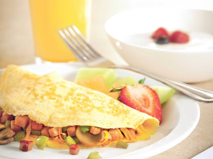 Un plato de desayuno con tortilla, verduras y un vaso de jugo de naranja.