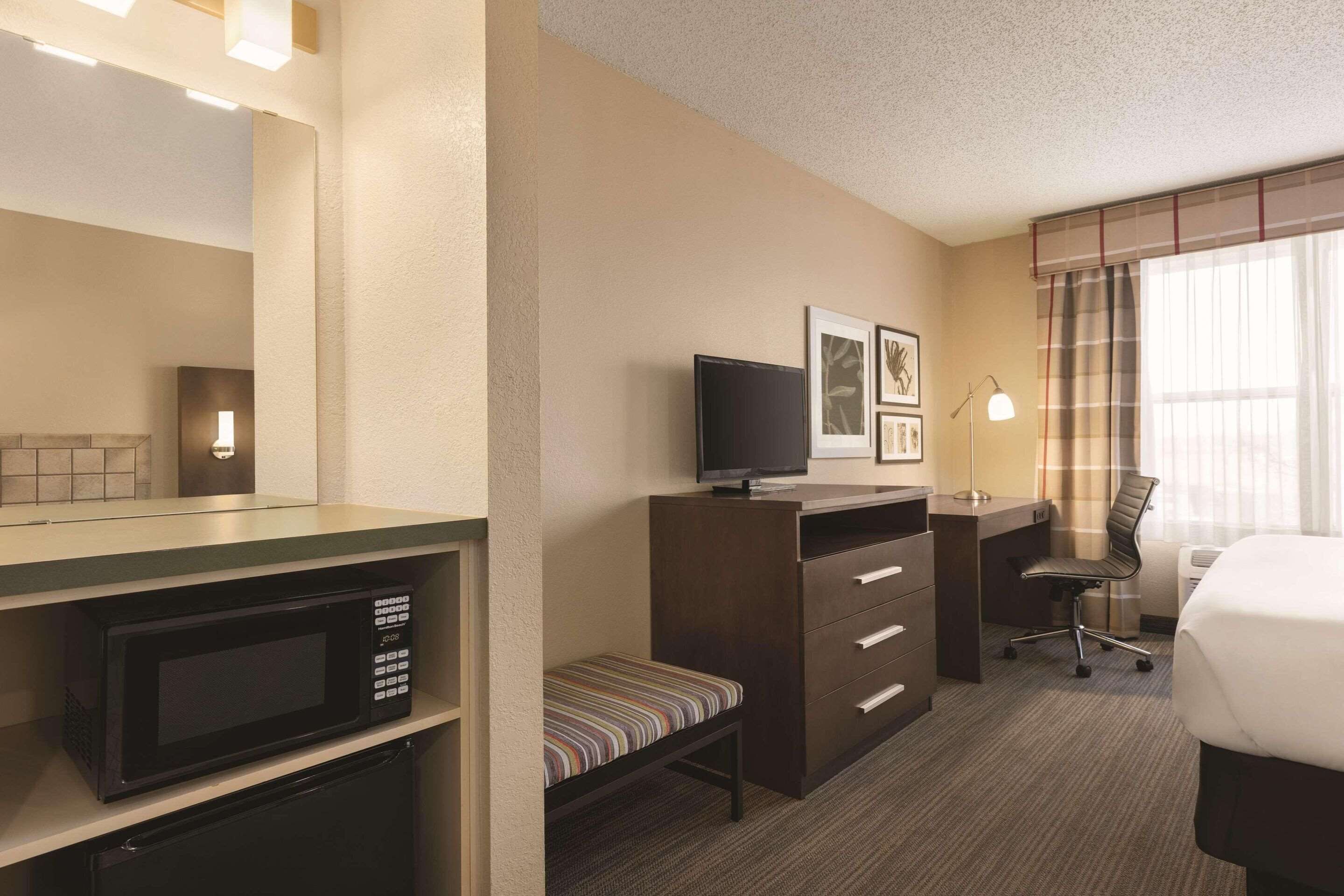 Une chambre d’hôtel équipée d’un four à micro-ondes, d’une petite banquette, d’un bureau avec une chaise, d’une télévision et d’un lit.
