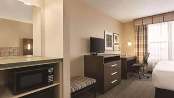 Une chambre d’hôtel équipée d’un four à micro-ondes, d’une petite banquette, d’un bureau avec une chaise, d’une télévision et d’un lit.