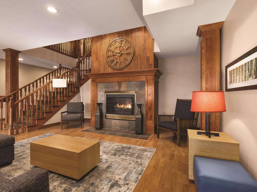 A spacious living room with a fireplace, wooden staircase, and a large clock on the wall.