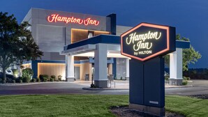 A Hampton Inn by Hilton hotel with a modern facade, illuminated signage, and a welcoming entrance.