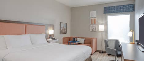 A hotel room with a large bed, a desk with a chair, a lamp, and a window with a view.