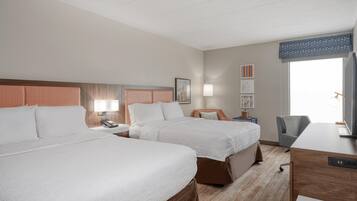 A hotel room with two beds, a desk, a chair, a TV, and artwork on the wall.