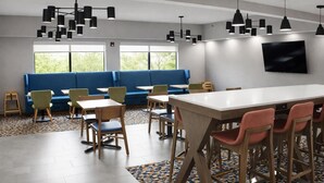 A modern dining area with a long table, multiple chairs, a blue sofa, and pendant lighting.