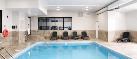 A swimming pool with a glass wall, chairs, and a lifebuoy.