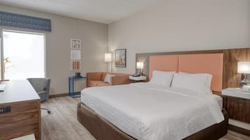 A hotel room with a large bed, a desk, a chair, a nightstand, and a window.