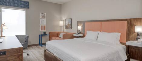 A hotel room with a large bed, a desk, a chair, a nightstand, and a window.