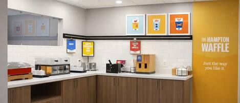 Una zona de cocina con estación de café y estación de waffles, y una pared con un letrero de The Hampton Waffle.