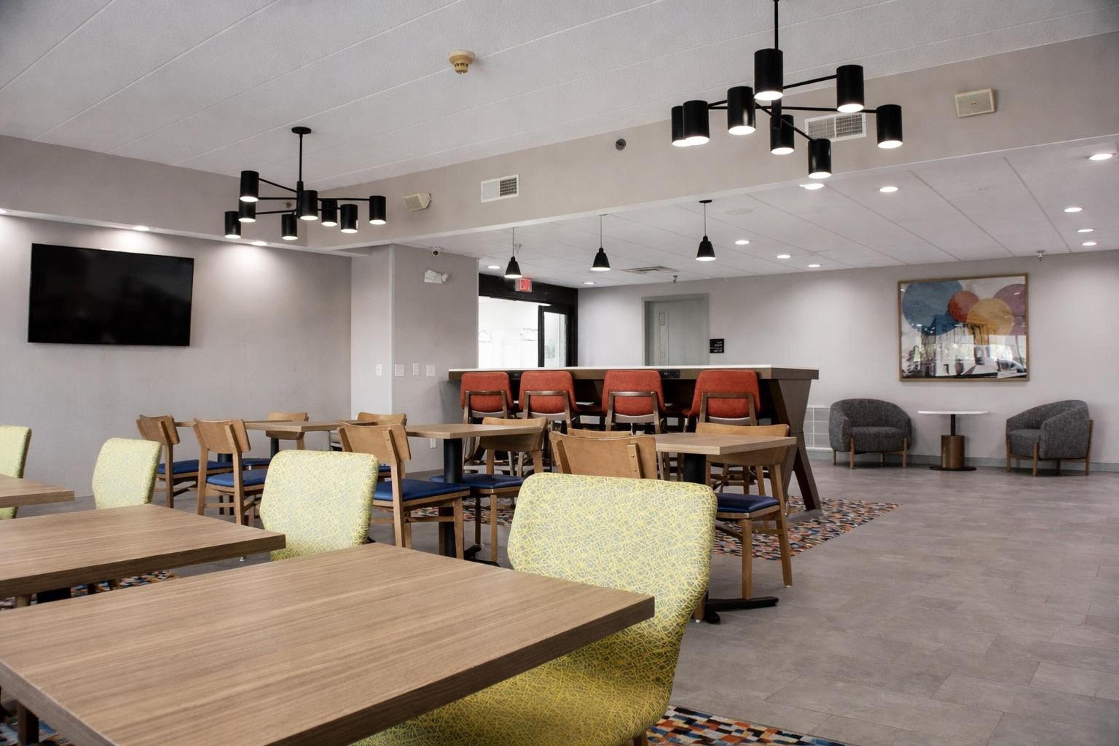 A conference room with multiple tables and chairs, ceiling lights, a flat-screen TV, and a large abstract painting on the wall.