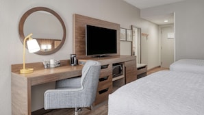 A hotel room with a wooden desk, a television, a chair, a bed, and a mirror.
