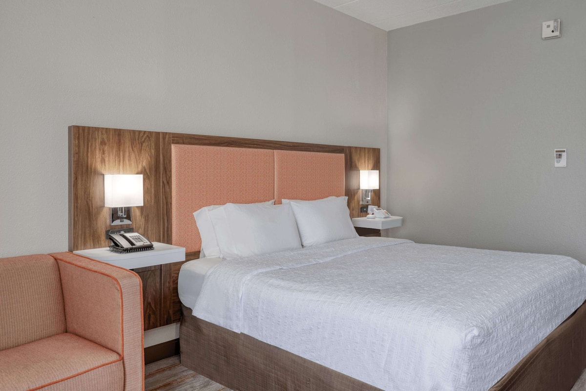 A hotel room with a large bed, a wooden headboard, two bedside tables with lamps, a telephone, and a small sofa.