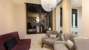 A modern living room with a purple sofa, two armchairs, and a large window with a view of the street.