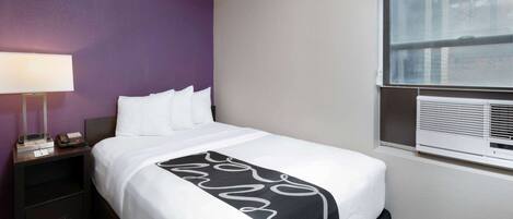 A hotel room with a bed, a nightstand, a lamp, and a window with blinds.