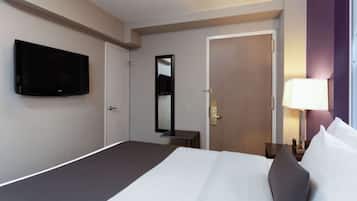 A hotel room with a bed, a TV, a mirror, a door, and a bedside table with a lamp.
