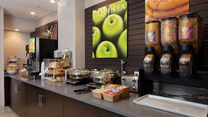 A breakfast buffet with various food items and a large poster of green apples.