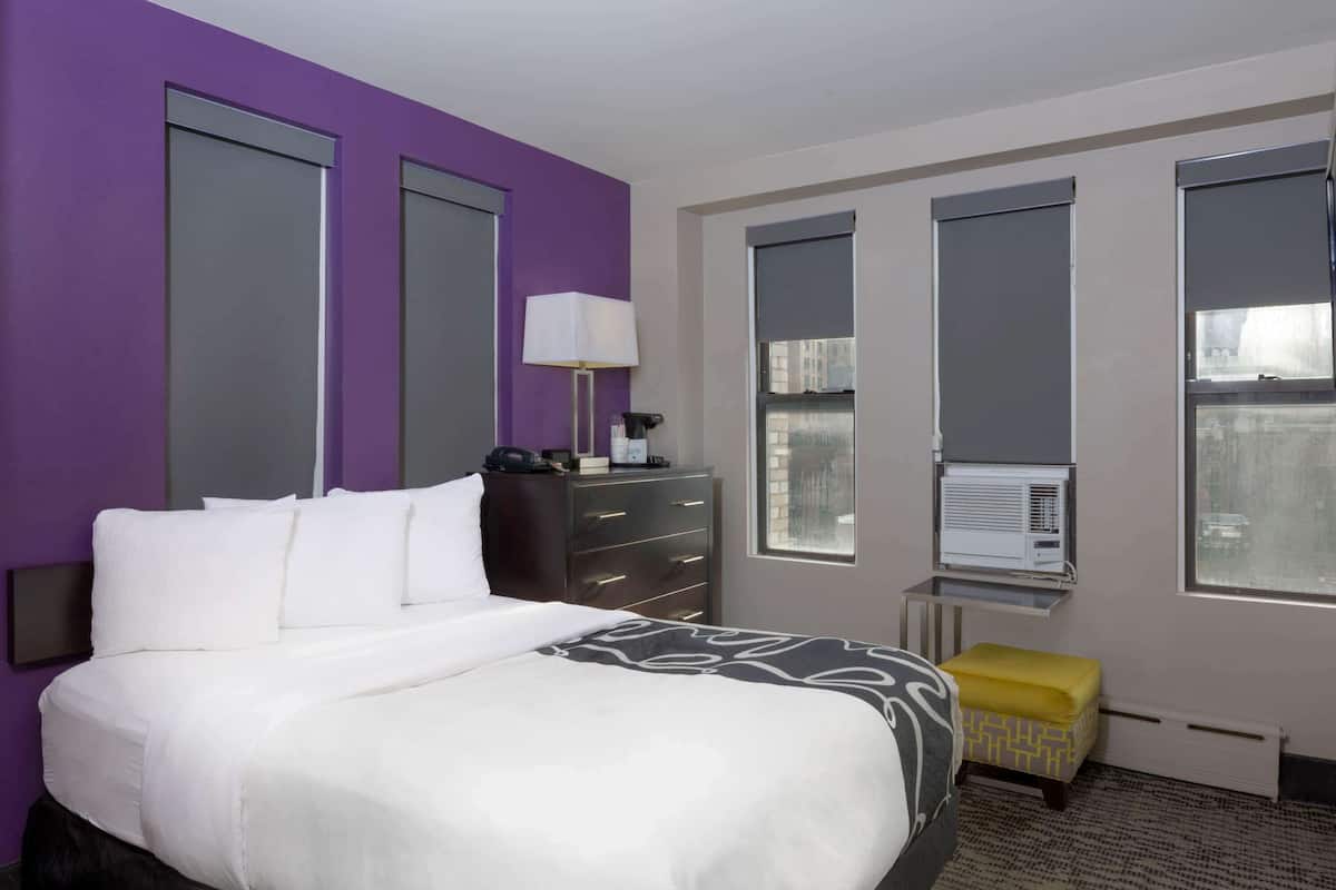 Une chambre d’hôtel équipée d’un lit, d’un bureau, d’une lampe, d’une fenêtre et d’un appareil de climatisation.