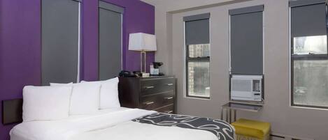 Een hotelkamer met een bed, een bureau, een lamp, een raam en een airconditioning.