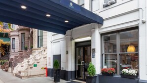A hotel entrance with a dark awning, a staircase, and flower planters on the sidewalk.