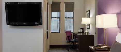 A hotel room with a bed, a desk, a chair, a TV, and a window.