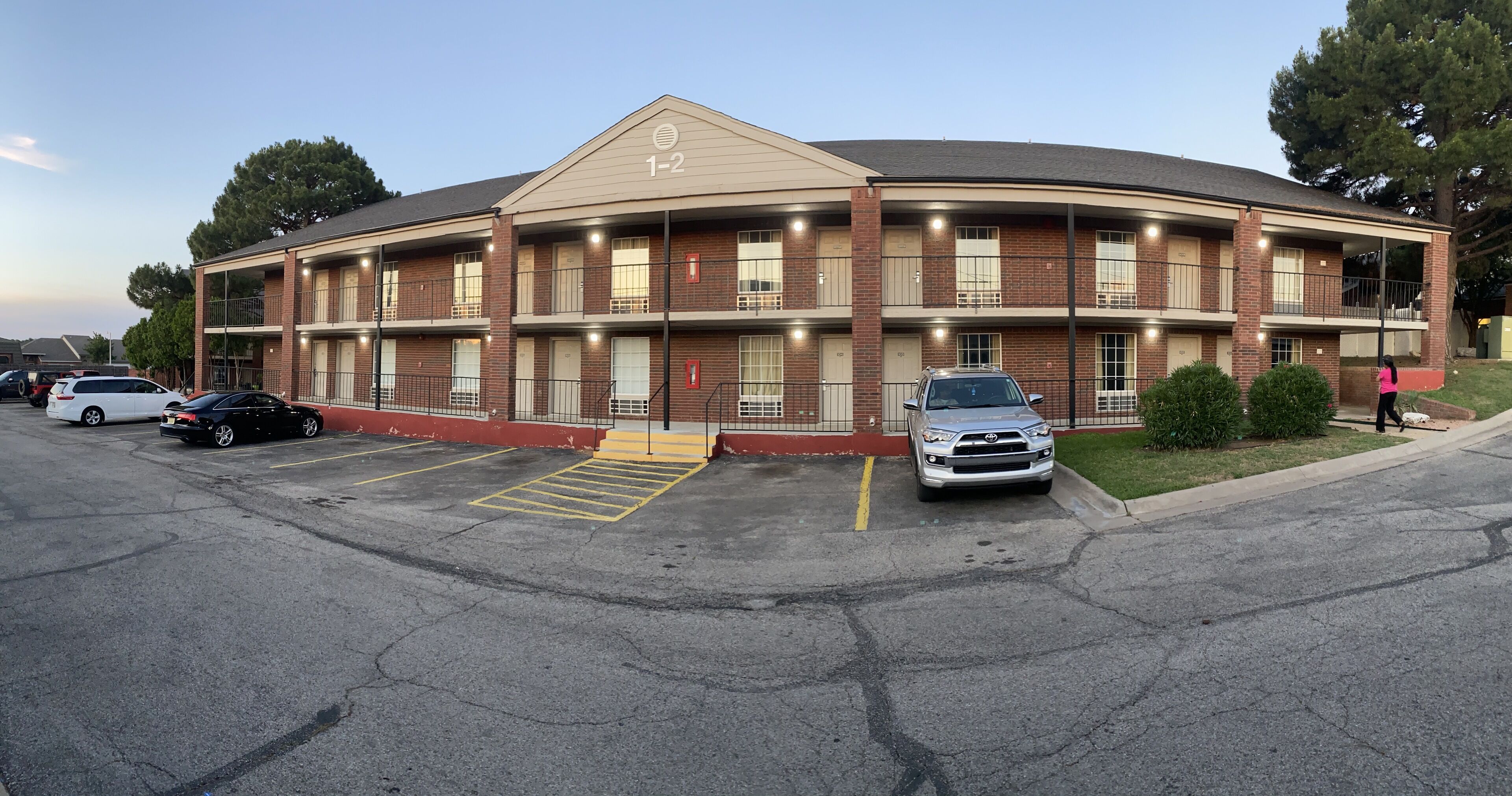 A multi-story building with a brick facade, numbered 1-2, featuring a central entrance with a ramp and a parking lot in front.