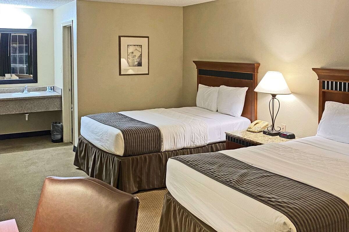 A hotel room with two beds, a desk, a chair, a lamp, and a picture on the wall.