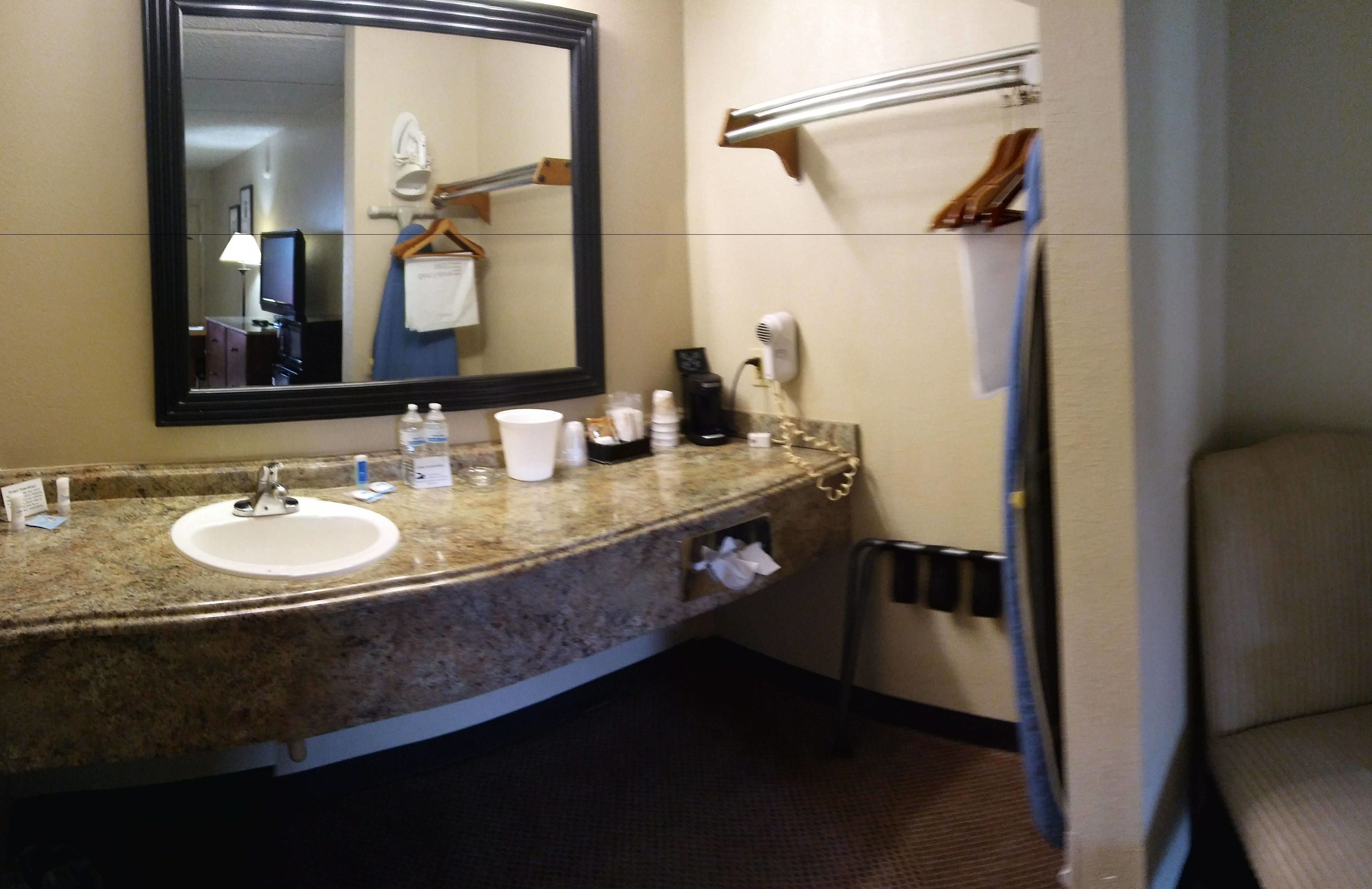 A bathroom with a granite sink, a mirror, a towel rack, a hairdryer, and a towel hanging on the wall.