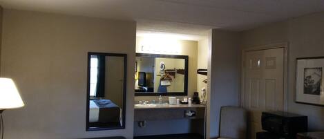 A hotel bathroom with a sink, mirror, and a chair.