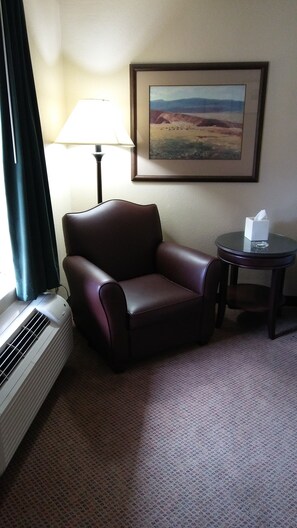 A hotel room with a leather armchair, a small round table with a tissue box, a lamp, and a painting on the wall.