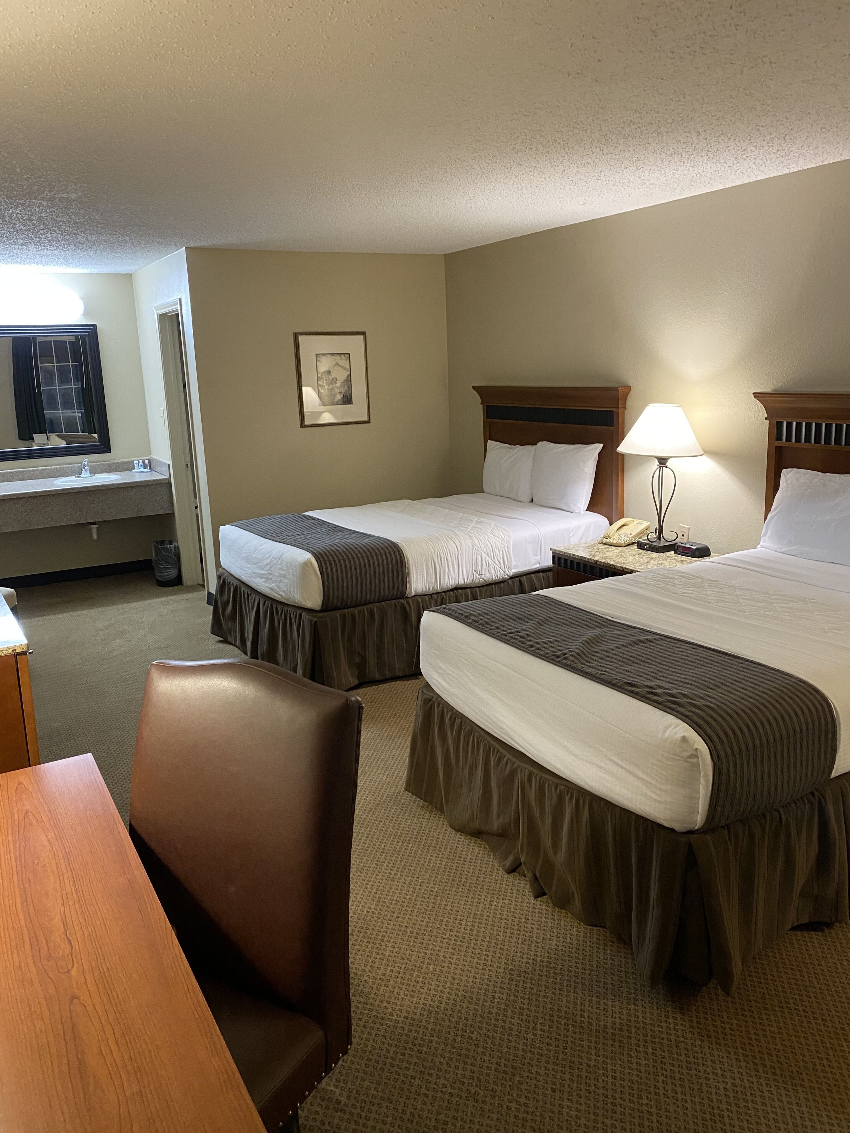 A hotel room with two beds, a desk, a chair, a lamp, and a telephone.