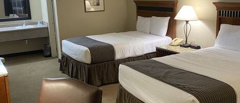 A hotel room with two beds, a desk, a chair, a lamp, and a telephone.
