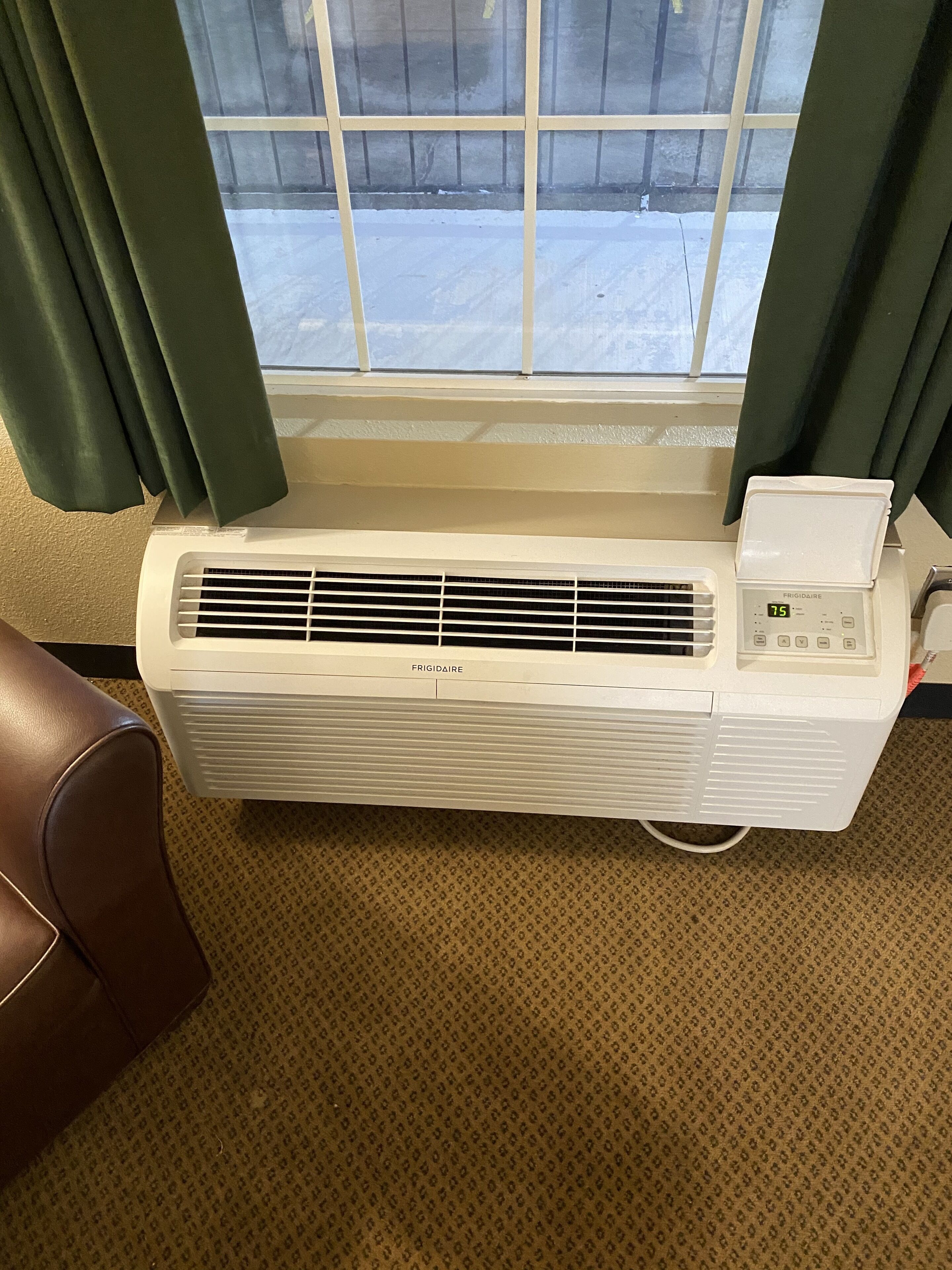 A white Frigidaire air conditioner unit mounted on a wall with a window above it.
