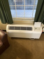 Un equipo de aire acondicionado Frigidaire blanco montado en una pared con una ventana encima.
